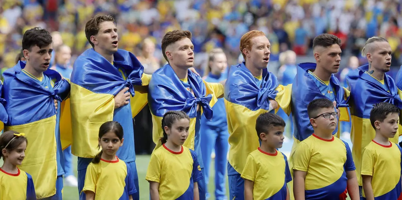 Los jugadores de la selecci&oacute;n ucraniana con la bandera de su pa&iacute;s atada al cuello entonan el himno nacional en su debut en la Eurocopa 2024 contra Ruman&iacute;a. EFE/EPA/RONALD WITTEK